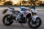 Ilustrasi AI motor BMW F 450 R 2027 bergaya naked sport dengan bodi putih, aksen biru merah, dan suspensi depan emas.