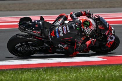Ilustrasi AI pembalap Aprilia MotoGP dengan motor hitam merah saat menikung ekstrem di lintasan balap.
