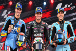 Ilustrasi AI tiga pembalap MotoGP mengenakan seragam balap dan topi Michelin sambil membawa helm di podium.